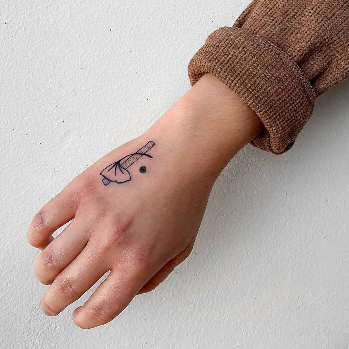Small hand tattoo of a leaf and dot on the back of a person's hand, wearing a brown sleeve.