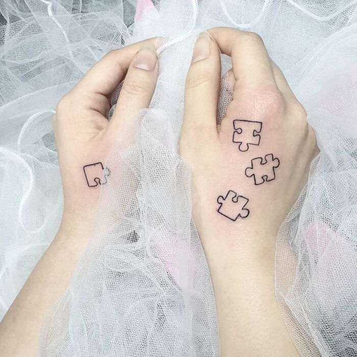 Small hand tattoos featuring puzzle pieces on both hands with delicate netting background.