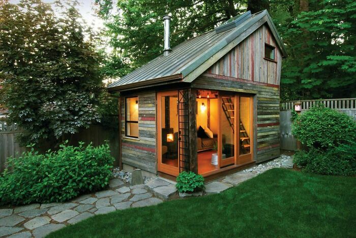 Small shed in a chic backyard with budget-friendly landscaping and cozy outdoor lighting surrounded by greenery.