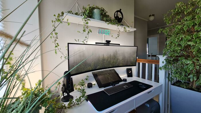 Cozy home office design with a curved monitor, greenery, and minimalist white desk for an inviting workspace.