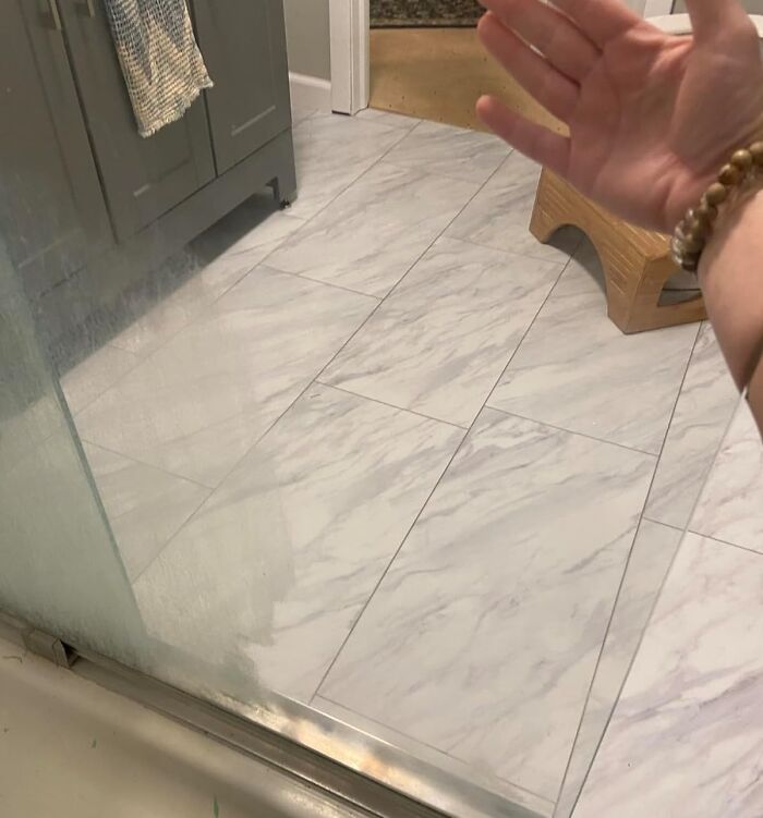 Hand gesturing towards clean bathroom floor, reflecting a successful pre-2025 cleaning mission.