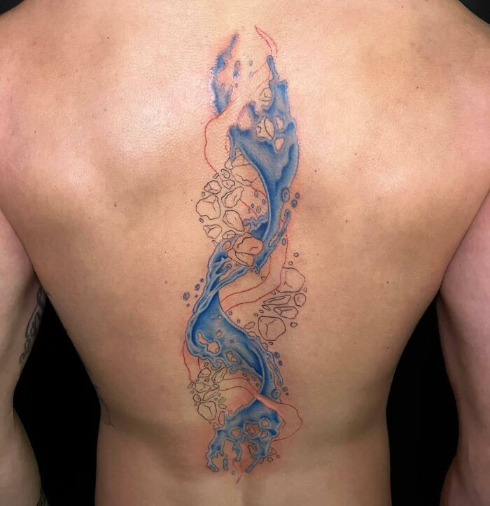 Colorful abstract spine tattoo design with blue and red elements, covering the center of a person's back.
