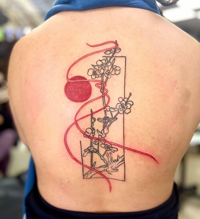 Delicate spine tattoo featuring cherry blossoms and a red sun design on a person's back.