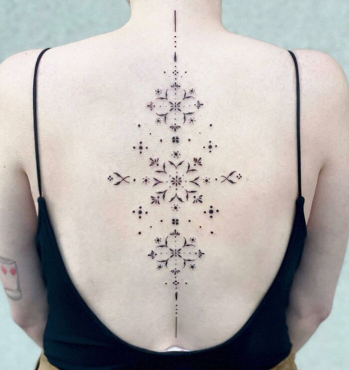Intricate floral spine tattoo on a woman's back, showcasing detailed symmetrical design.