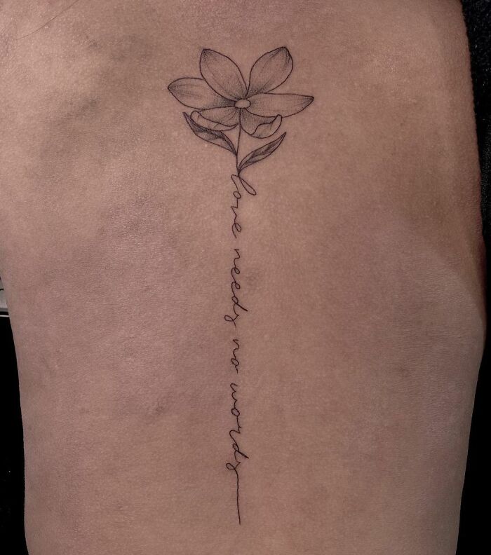 Delicate flower spine tattoo with script "love needs no words" detailing a meaningful design.