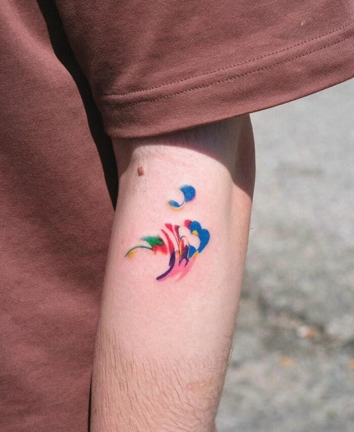 Abstract tattoo in vibrant colors on forearm, showcasing self-expression through artistry.