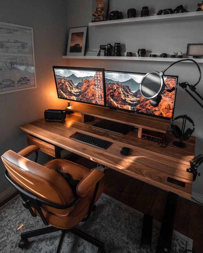 Cozy home office design with dual monitors, wooden desk, brown leather chair, ambient lighting, and camera gear on shelves.