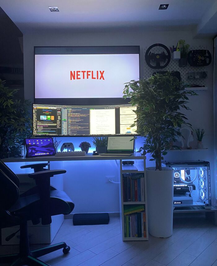 Modern home office design with multiple monitors, ambient lighting, plants, and a cozy work setup featuring a gaming chair.