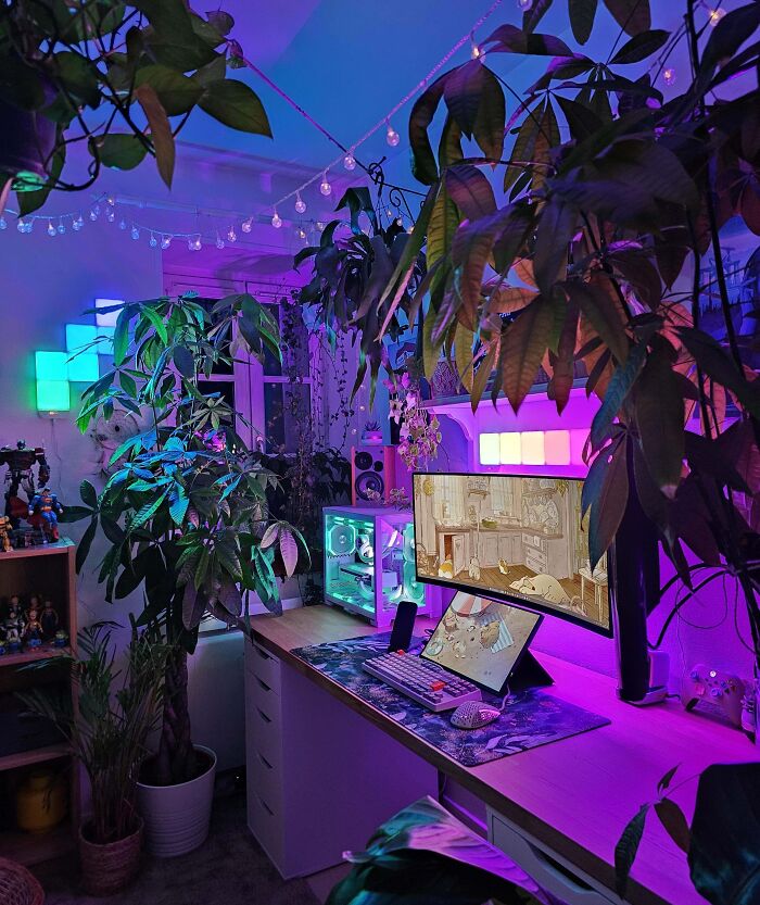 Cozy home office design with vibrant LED lighting, lush green plants, and a modern computer setup on a spacious desk.