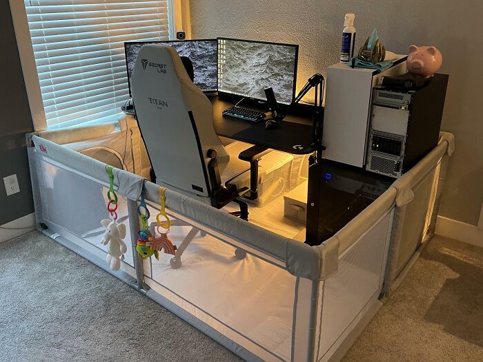 Home office design featuring a gaming chair, dual monitors, and a surrounding playpen for a cozy workspace.
