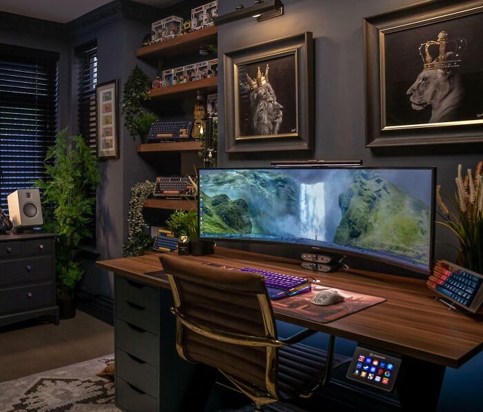 Cozy home office design with a large curved monitor, wooden desk, leather chair, plants, and framed wall art.