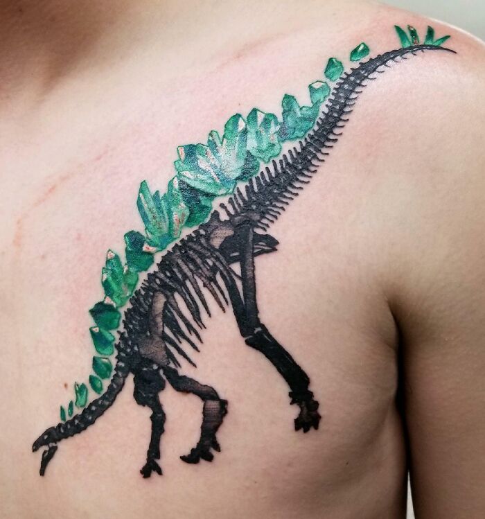 Green and black dinosaur tattoo on a person's shoulder, showcasing creative tattoo design.