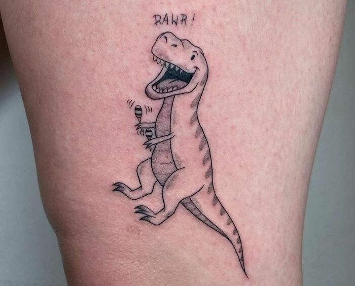 Cartoon dinosaur tattoo with microphone and the text "RAWR!" on skin.