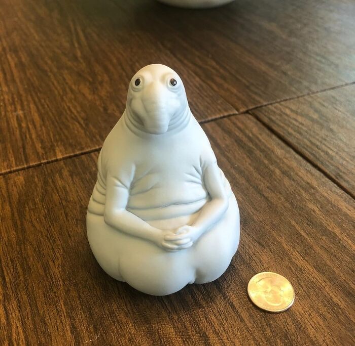 Humorous figurine with a quirky expression beside a coin on a wooden table, highlighting funny products.