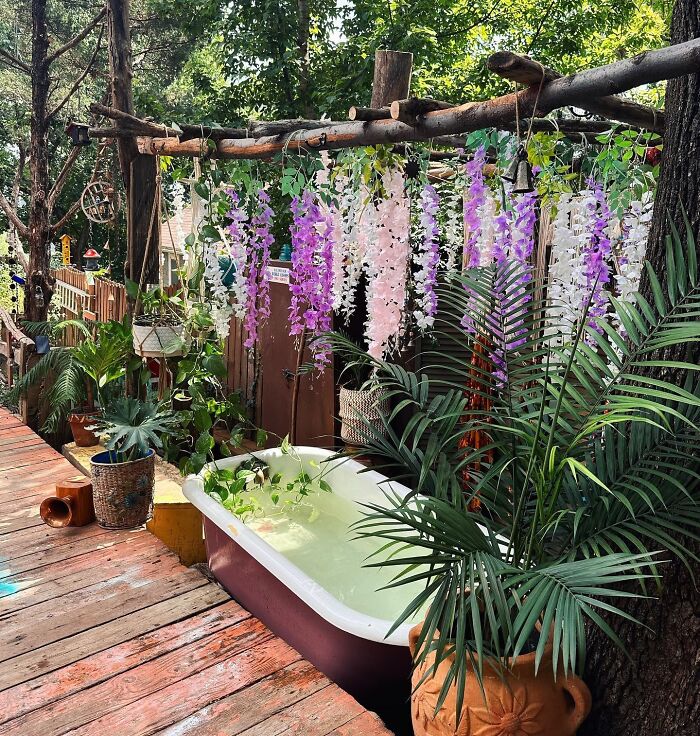 Colorful DIY bathtub surrounded by lush plants and hanging flowers, creating a chic backyard outdoor space.