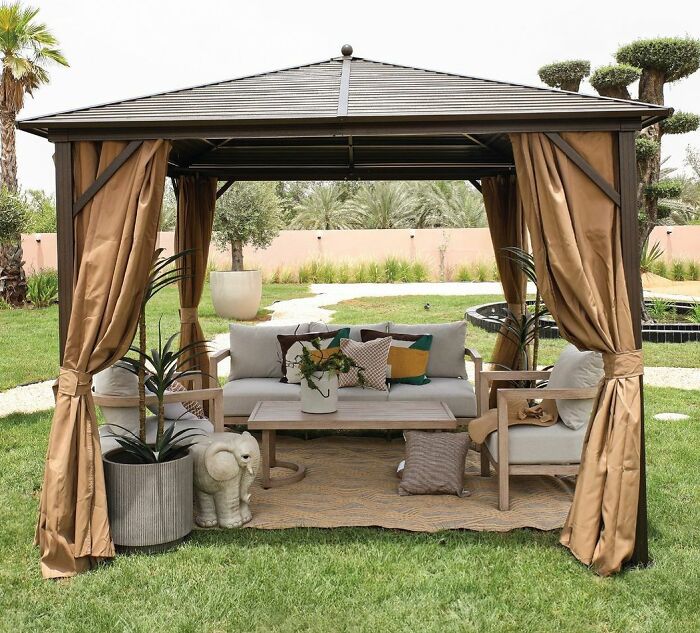 Brown gazebo with cozy seating and plants in a massive backyard, showcasing chic outdoors and backyard ideas.