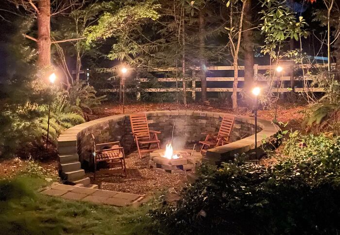 Cozy backyard conversation pit with fire pit and wooden chairs surrounded by stone seating for chic outdoors ambiance.
