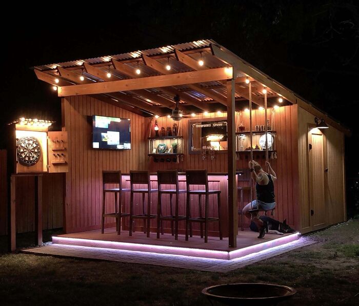 Colorful modern backyard bar with string lights and wooden stools, creating a chic outdoors space for entertaining.