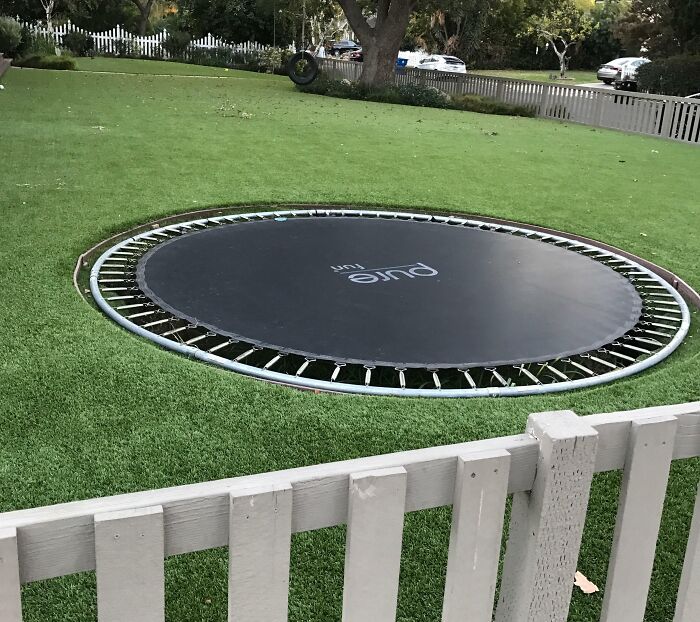 Inground trampoline set in a spacious backyard with green grass and a white fence for chic outdoors design ideas.