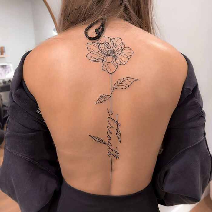 Back with a floral spine tattoo featuring the word "strength," showcasing elegant tattoo design work.