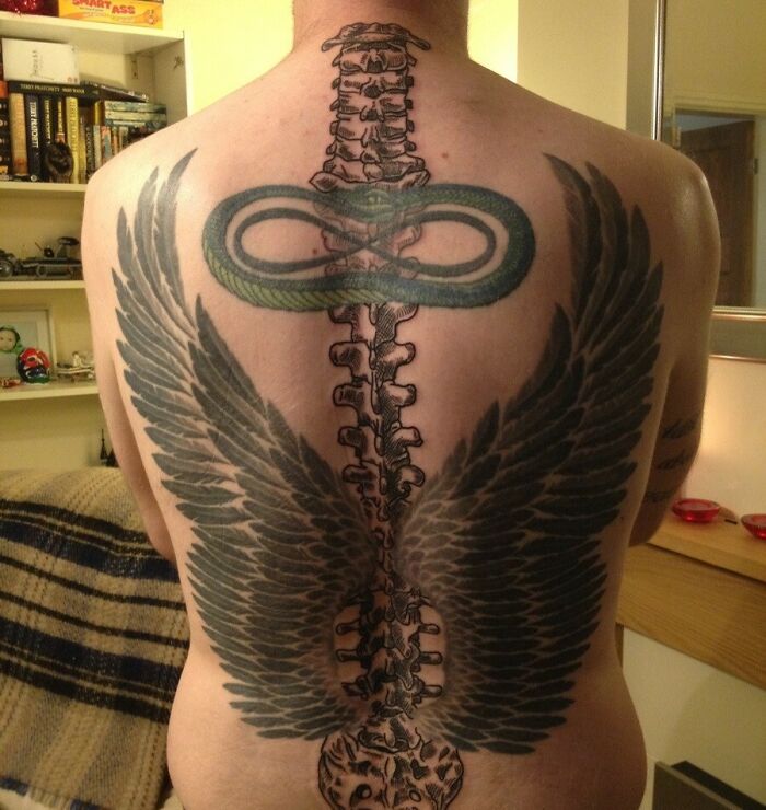 Back with a detailed spine tattoo featuring wings and a green snake wrapping around the vertebrae.