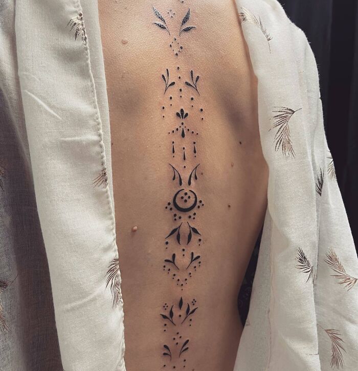 Elegant spine tattoo with intricate patterns, displayed on a person's back draped in a light garment.