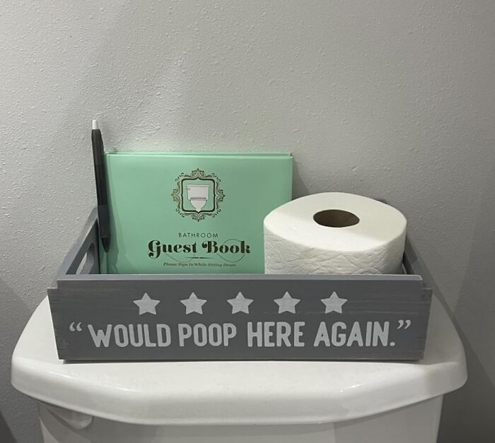 Bathroom guestbook and toilet paper with humorous sign, "Would p**p here again," in a quirky bathroom setting.