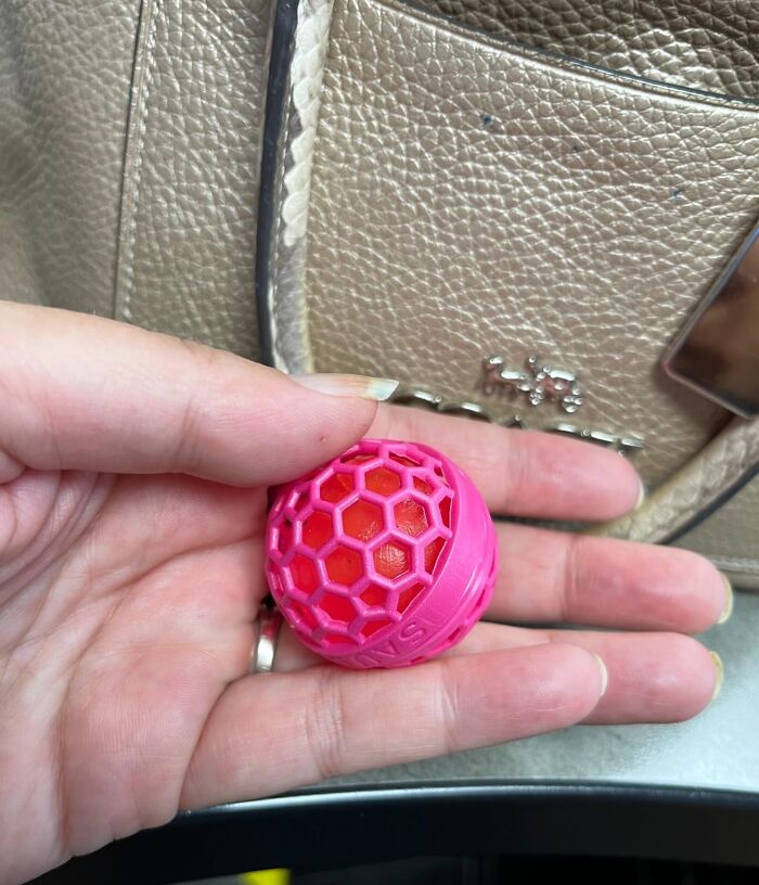 Hand holding a pink and red ball in front of a textured bag, symbolizing 2025 success and pursuing goals today.