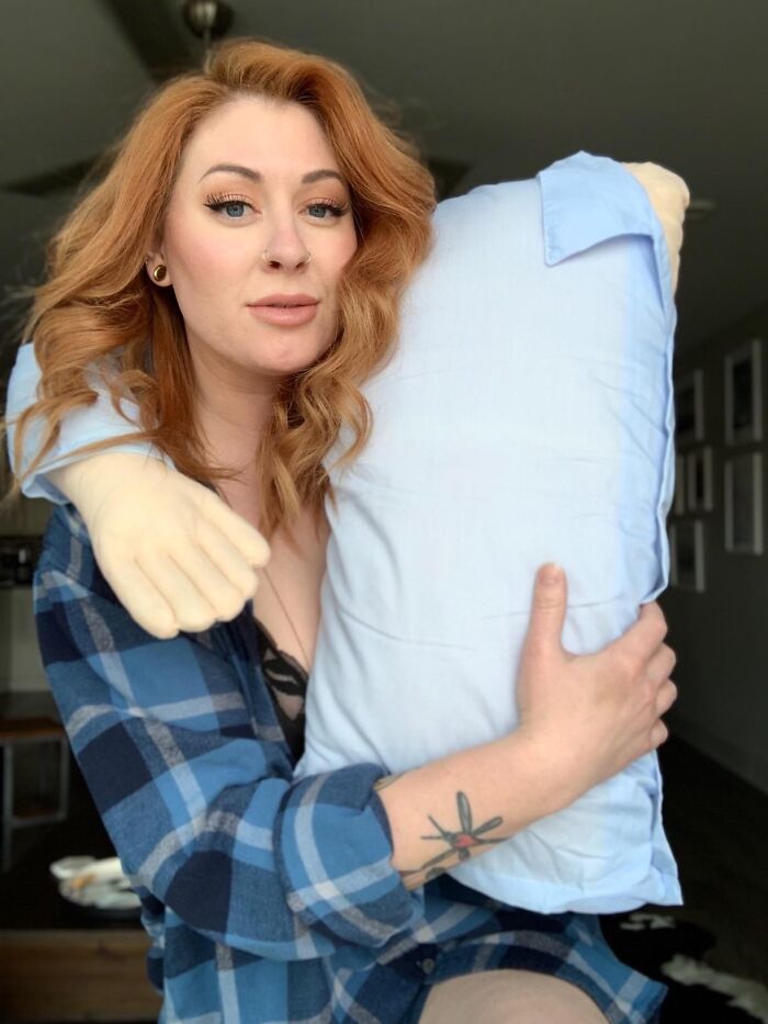 Woman in blue plaid shirt holding a quirky novelty pillow shaped like a man's arm, perfect for Christmas gifts.