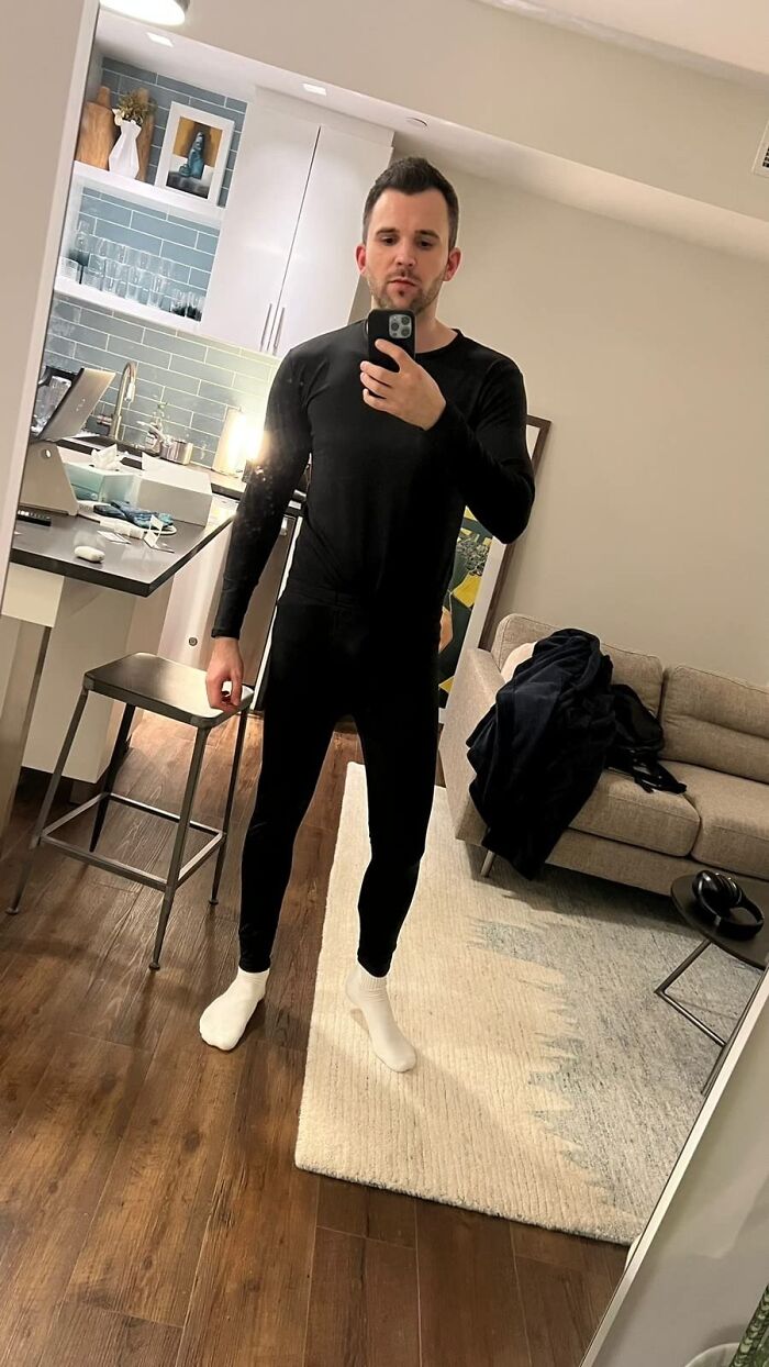 Man in a black outfit and white socks taking a mirror selfie in a modern apartment, ideal for unique gift inspiration.