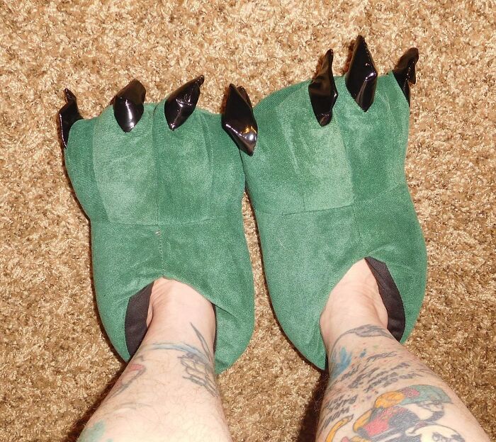 Green monster claw slippers on tattooed legs, adding humor to any outfit.