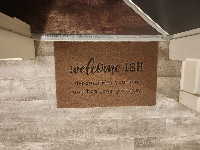 Funny doormat with "welcome-ISH, depends who you are" text on wooden floor.