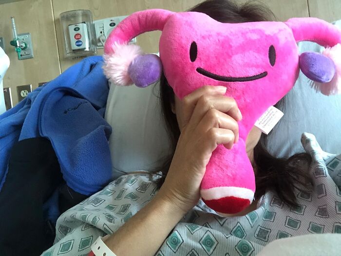 Person holding a funny uterus-shaped plush toy to their face in a playful hospital setting.