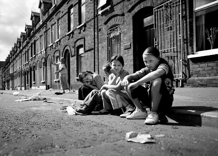 Black and white photo of children sitting on a street curb in an urban setting capturing urban magic in photography awards.