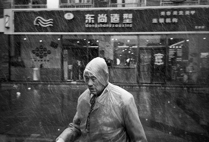 Man wearing raincoat walking in heavy rain capturing urban magic in a black and white street photography scene.