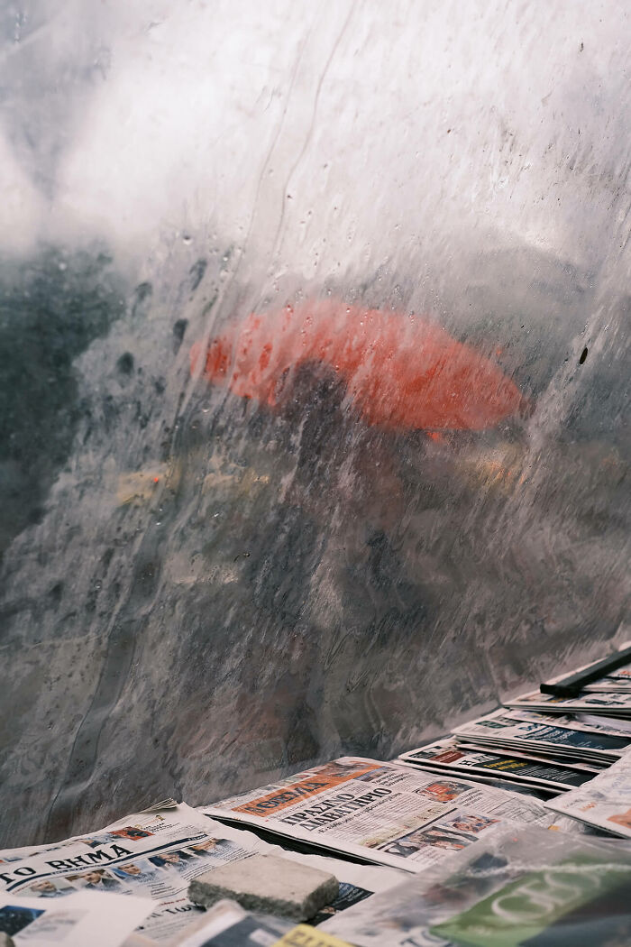 Person with a red umbrella seen through a rain-covered window, capturing urban magic in a rainy city scene.