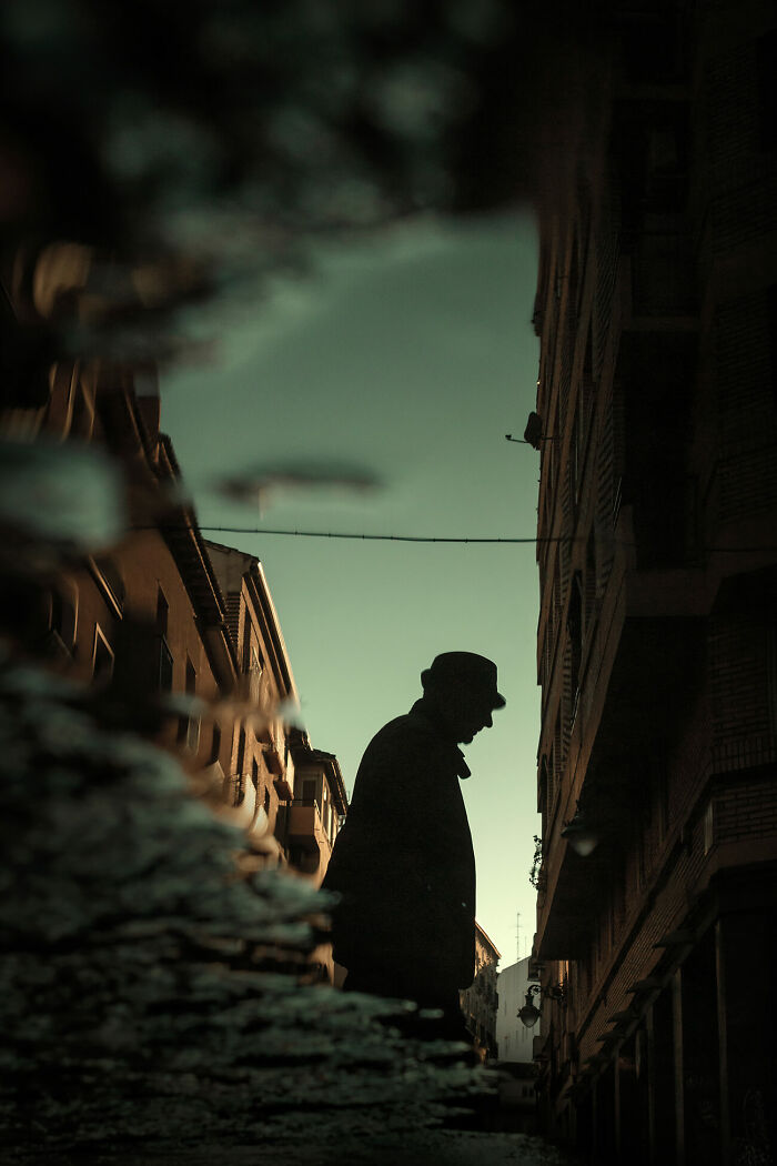 Silhouette of a man in a hat walking down an urban street at dusk, capturing urban magic in street photography.