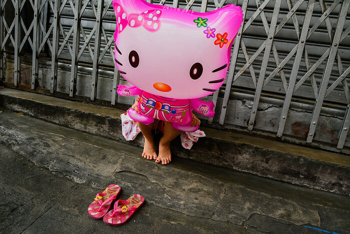 Child holding a large pink balloon in urban setting showcasing vibrant street photography capturing urban magic.