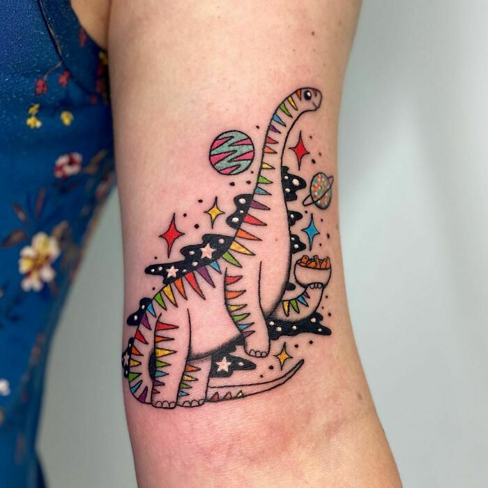 Colorful dinosaur tattoo with cosmic elements on an arm, showcasing a creative tattoo idea.