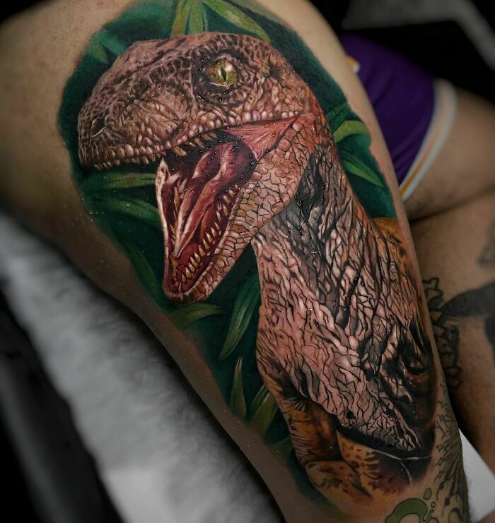 A detailed dinosaur tattoo with vibrant colors and realistic textures on a person's leg.