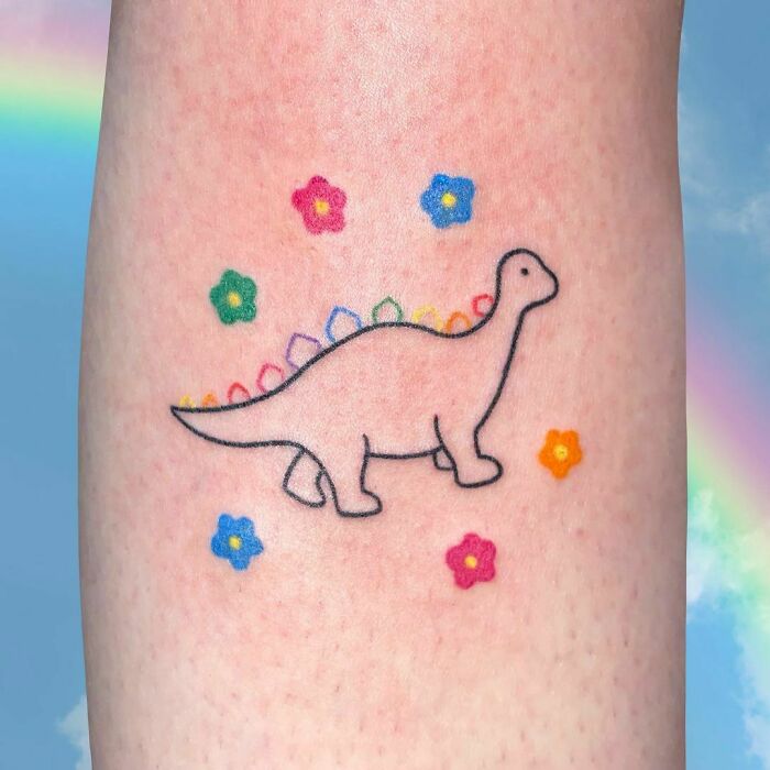 Colorful dinosaur tattoo with flowers, featuring a simple design on skin with a rainbow background.