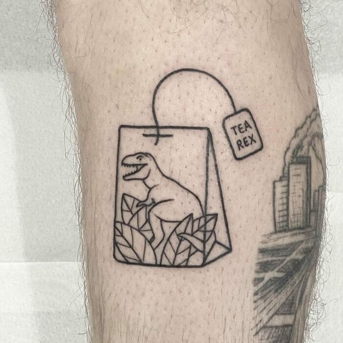 Tattoo of a dinosaur in a teabag labeled "Tea Rex," showcasing a cool dinosaur tattoo idea on skin.