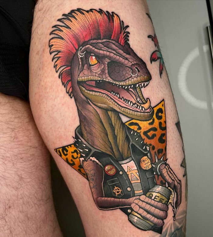 Colorful dinosaur tattoo with a punk theme featuring a mohawk and leather vest on a person's leg.