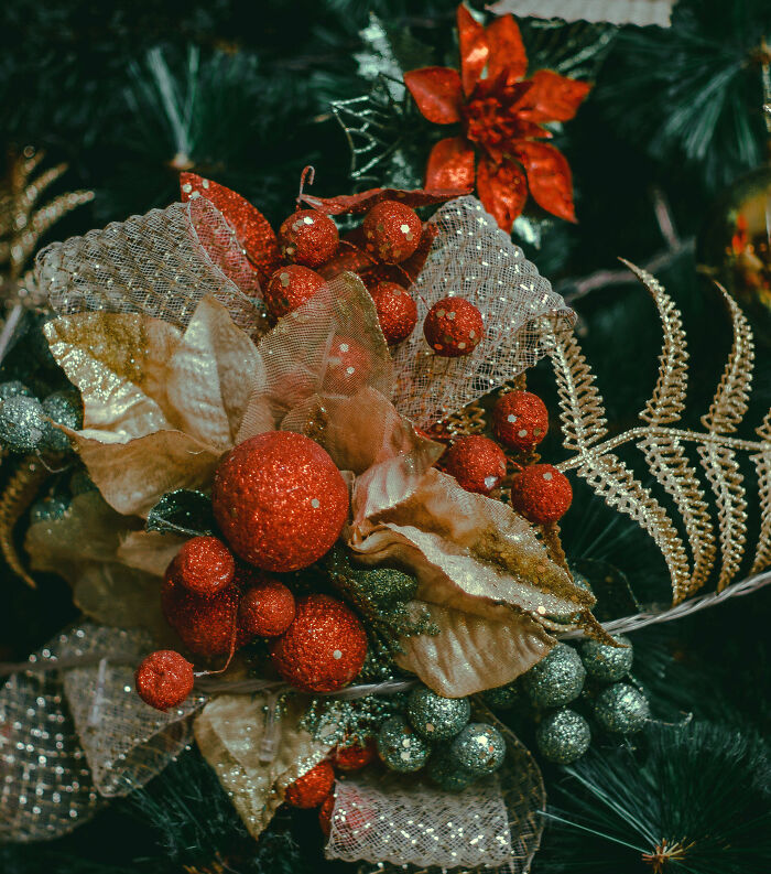 Red silk flowers and glittery berries decorating a Christmas tree for affordable Christmas decor ideas 2024.