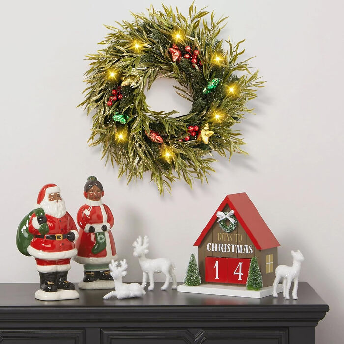 Christmas decor affordable with festive wreath, Santa figurines, reindeer, and countdown calendar on black surface against white wall.