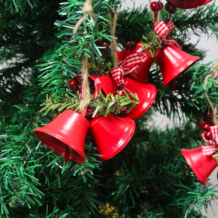 Red Christmas bells hanging on green tree branches as affordable Christmas decor ideas for 2024 celebrations.