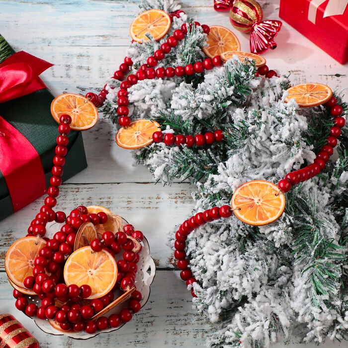 Citrus garlands with red beads decorating snowy fir branches as affordable Christmas decor ideas for 2024.
