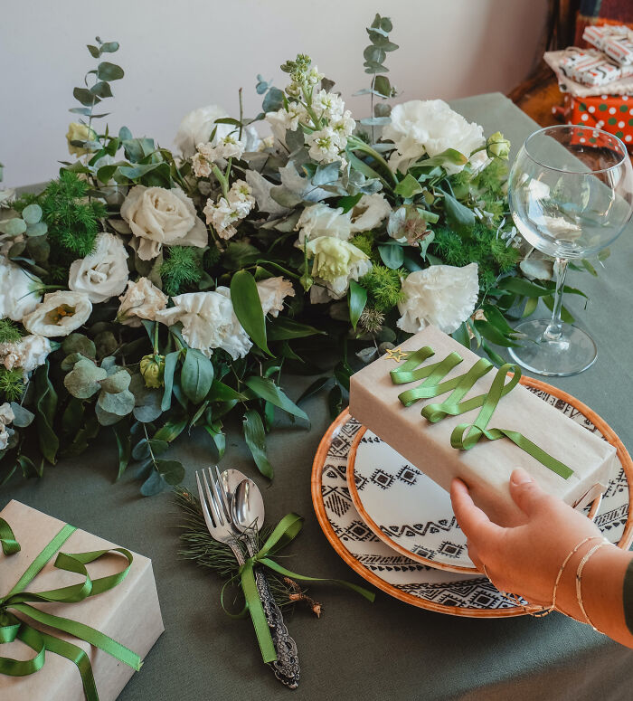 Affordable Christmas decor with wrapped presents on a festive table setting featuring greenery and white flowers.