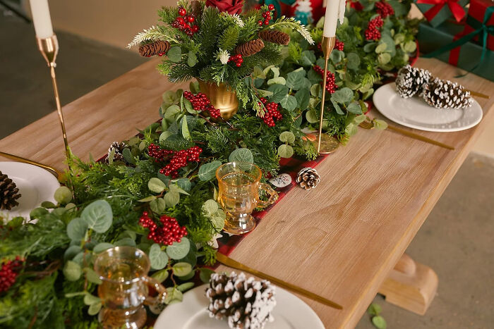 Pine garland with berries, candles, and pine cones on a wooden table showcasing affordable Christmas decor ideas.