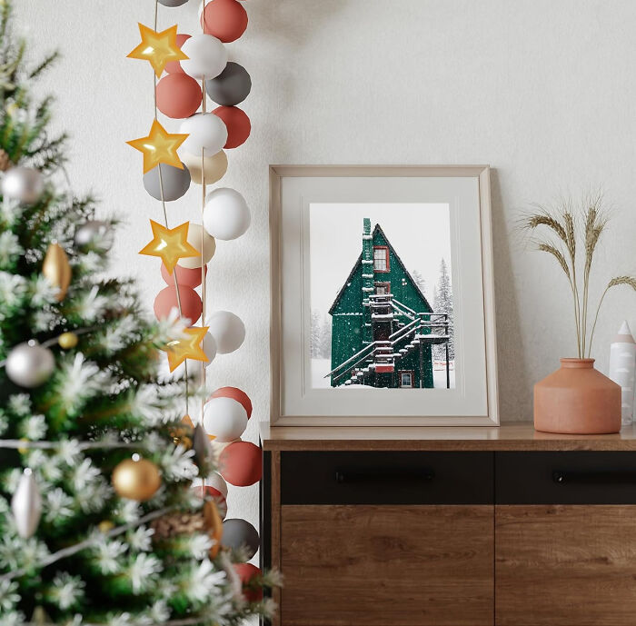 Christmas poster on a wooden dresser with affordable Christmas decor ideas featuring festive garland and a decorated tree.